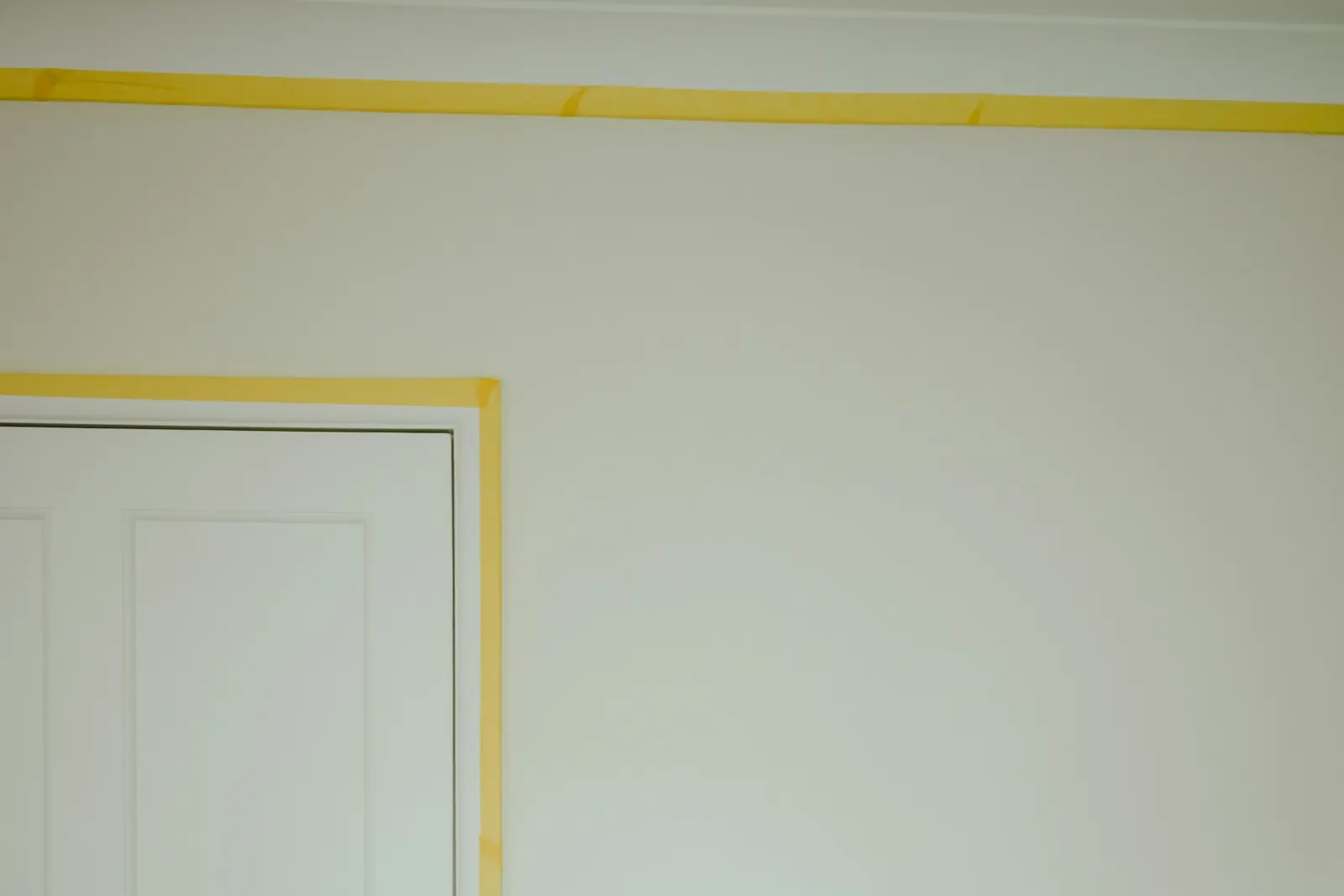 Witte muur met een strak afgeplakte deurlijst, klaar voor de laatste laag