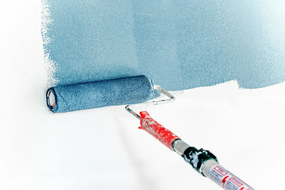 Verfroller zet een egale laag blauw op een witte muur